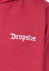 Rød sweatshirt med en hvid broderet "Dropsize" logo i gotisk skrifttype, lavet af blødt bomuldsmateriale med en glat tekstur.