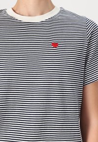 T-shirt rayé en coton bleu marine et blanc, avec un petit cœur brodé rouge sur la poitrine gauche. Encolure ronde côtelée et manches courtes.