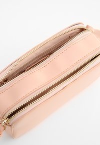 Rosa läderväska med tre zippered fack och guldhardware, med en jämn textur och rektangulär form.