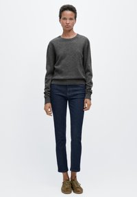 Grauer Pullover mit langen Ärmeln, kombiniert mit dunkelblauen Skinny-Jeans und braunen Schnürschuhen. Das Outfit zeichnet sich durch ein schlichtes, funktionales Design aus.