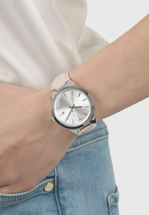 Silver wristwatch with beige leather strap, round dial showing 2:36, worn on left wrist above blue denim jeans pocket.