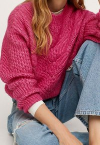Pull en tricot fuchsia avec un motif texturé, doté d'un col rond et d'épaules tombantes. Associé à un jean bleu clair usé.
