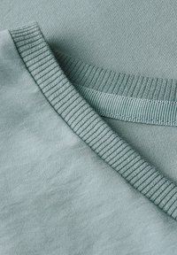 Tessuto blu acciaio chiaro con scollo a coste e morbida texture, che mostra sottili variazioni tonali sulla superficie.