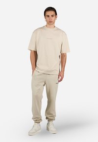 Beige bomull T-skjorte med korte ermer og rund hals, paret med matchende beige joggebukser. T-skjorten har subtil merking på brystet.
