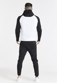 Felpa con cappuccio con maniche e schiena nere, parte anteriore bianca, pantaloni neri aderenti e sneakers bianche. Tessuto testurizzato e design casual.