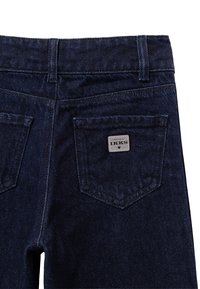 Ciemnoniebieskie dżinsy z wysokim stanem, posiadające dwie tylne kieszenie oraz srebrną metkę z napisem "IKKS" wszytą na prawej kieszeni. Teksturowana tkanina.