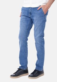 Jeans in denim azzurro chiaro con una vestibilità slim, dotati di cinque tasche e cuciture sottili. Abbinati a sneaker nere e una camicia bianca con bottoni.