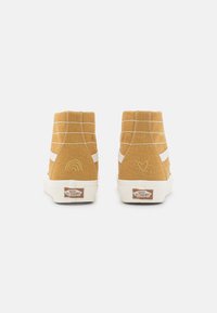 Högskoade sneakers i senapsgul canvas med vita sidremsor. Har broderade regnbågs- och hjärtmotiv på hälen. Vit gummisula.