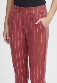 Pantaloni a righe rosse con una consistenza morbida, caratterizzati da strisce verticali bianche, pieghe davanti e tasche laterali. Vita elastica.