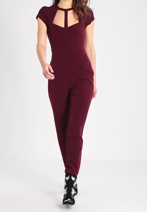 Combinaison bordeaux avec manches courtes type casquette, encolure découpée, silhouette ajustée et jambes fuselées, associée à des chaussettes noires à motifs.