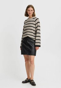 Suéter de punto beige con rayas negras, textura acanalada y mangas largas, combinado con una minifalda de cuero negra y mocasines negros con detalles dorados.
