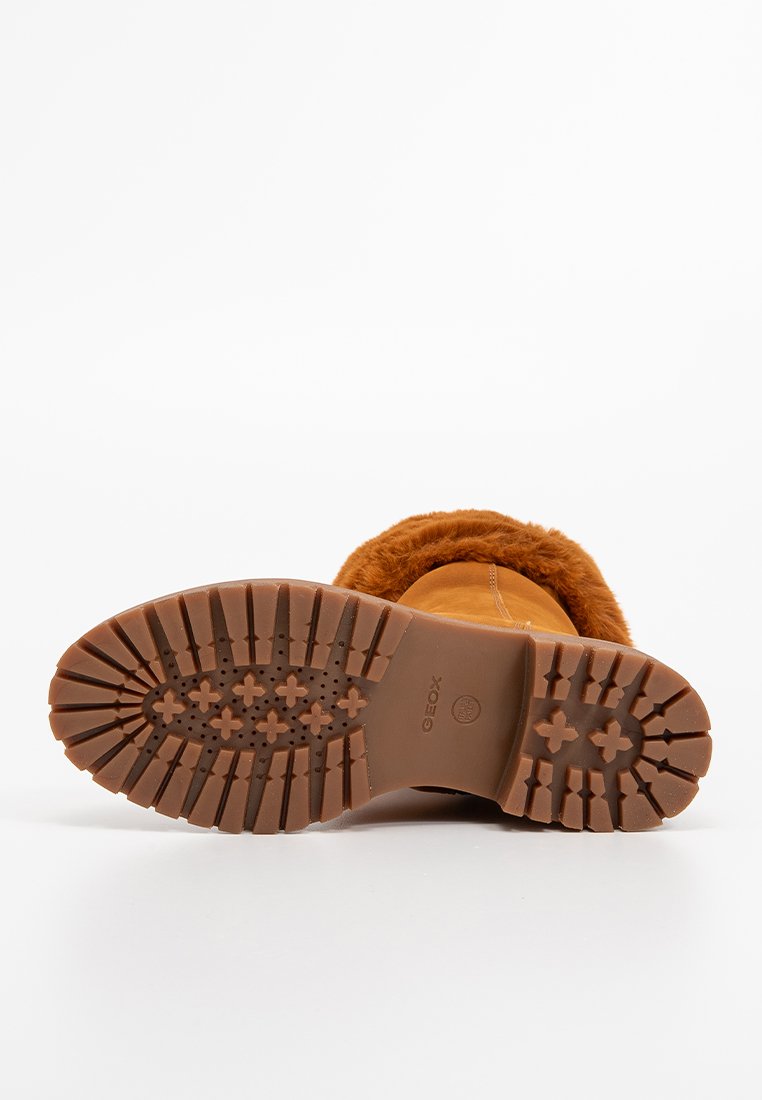 Bota de invierno marrón con suela gruesa y antideslizante y forro de piel, mostrando el patrón de agarre y el nombre de la marca sobre fondo blanco.