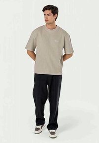 Camisa bege de mangas curtas, com gola redonda e textura canelada, combinada com calças largas pretas e ténis multicoloridos. Design simples, sem padr�ões.