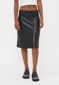 Svart skinnimitation kjol med en pennform, med en framtill slits, sydda detaljer och en slät yta. Bärs med svarta loafers.