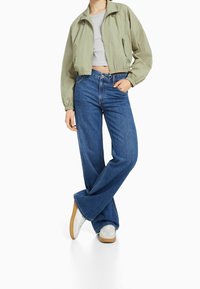 Cropped green jacket, gray top, and wide-leg blue denim jeans with light distressing, paired with white sneakers and gum soles.