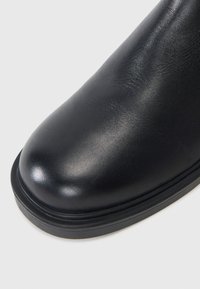 Black leather boot with a smooth, glossy finish. Rounded toe shape, featuring a sturdy black rubber sole.