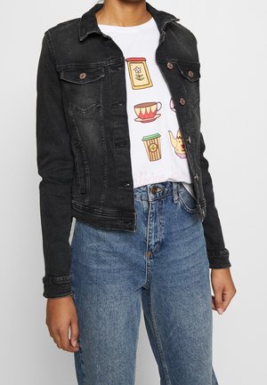 Persona que lleva una chaqueta vaquera negra sobre una camiseta blanca con ilustraciones coloridas temáticas de café y vaqueros azules.