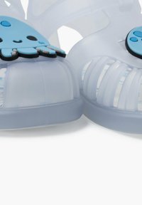 Translucent blue sandals with a rounded design, featuring a playful blue octopus accent and textured, open-toe ventilation slots.
