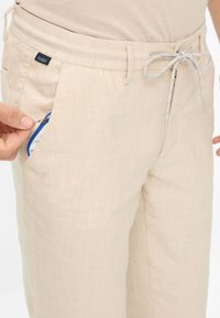 Beige pants made of lightweight fabric with a drawstring waist and a zippered front pocket featuring a blue zipper.