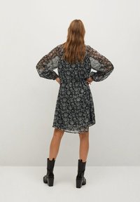 Czarna sukienka z przezroczystymi, długimi rękawami w kwiatowy wzór; do kolan, o luźnym kroju. Zestawiona z czarnymi botkami na obcasie sięgającymi do kostki.