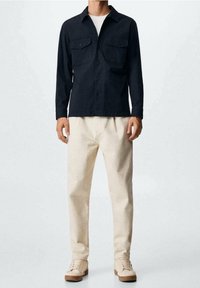 Granatowa koszula z guzikami, z dwoma kieszeniami na piersi, w połączeniu z kremowymi spodniami i jasnobeżowymi trampkami. Gładka tkanina, luźny krój.