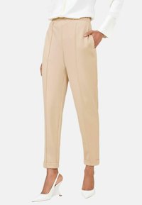 Beige gepersonaliseerde broek met een rechte pasvorm, voorzien van verticale zakken, een vlakke tailleband en opgerolde manchetten. Draag met witte hakken.