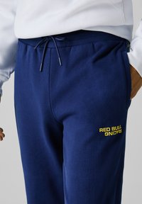 Navyblaue Sweatpants aus weichem Stoff, mit elastischem Bund und Kordelzug sowie einem gelben "RED BULL RACING"-Logo an der Seite.