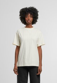 Camiseta de algodón amarilla clara con un ajuste relajado, mangas cortas y rayas blancas. Presenta un logo bordado en el pecho.