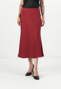 Jupe bordeaux midi en tissu lisse avec un ourlet évasé, assortie à des chaussures à talons noirs. Design simple et élégant.