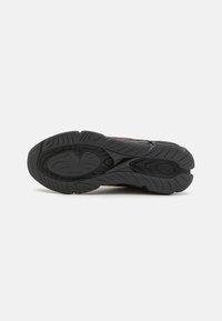 Semelle de chaussure de sport noire avec une adhérence en caoutchouc texturé, présentant des rainures et des crêtes pour une meilleure traction, avec un accent orange près du centre.