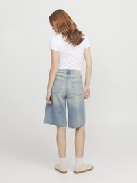 Ανοιχτό μπλε τζιν σορτς bermuda με χαλαρή εφαρμογή, πέντε τσέπες και σκληρές άκρες. Συνδυασμένα με λευκές κάλτσες και μπεζ αθλητικά παπούτσια.