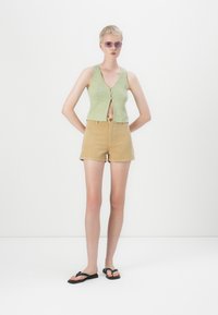 Green cropped tank top with button closure and beige corduroy shorts, paired with black flip-flops; minimalist design on white background.