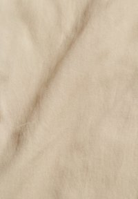 Tissu beige avec une fine texture côtelée diagonale et des plis subtils créant des ombres douces et des reflets.