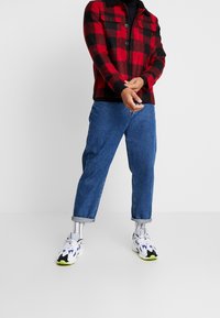 Rød og sort rutet skjortejakke med trykknapper, sort krave, parret med blå denimjeans og farverige sneakers med hvide detaljer.