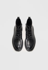 Botas tobilleras de cuero negro con un panel texturizado, puntera redonda, suelas planas y sistema de cordones. Cuentan con cremalleras laterales para facilitar su uso.