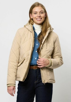 Giacca trapuntata beige con cappuccio, dotata di tasche laterali e polsini a costine, indossata sopra una camicia di denim, ambientata su uno sfondo chiaro.