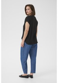 Haut noir à manches courtes avec une coupe décontractée, associé à un jean bleu ample et des chaussures plates noires, vu de dos.