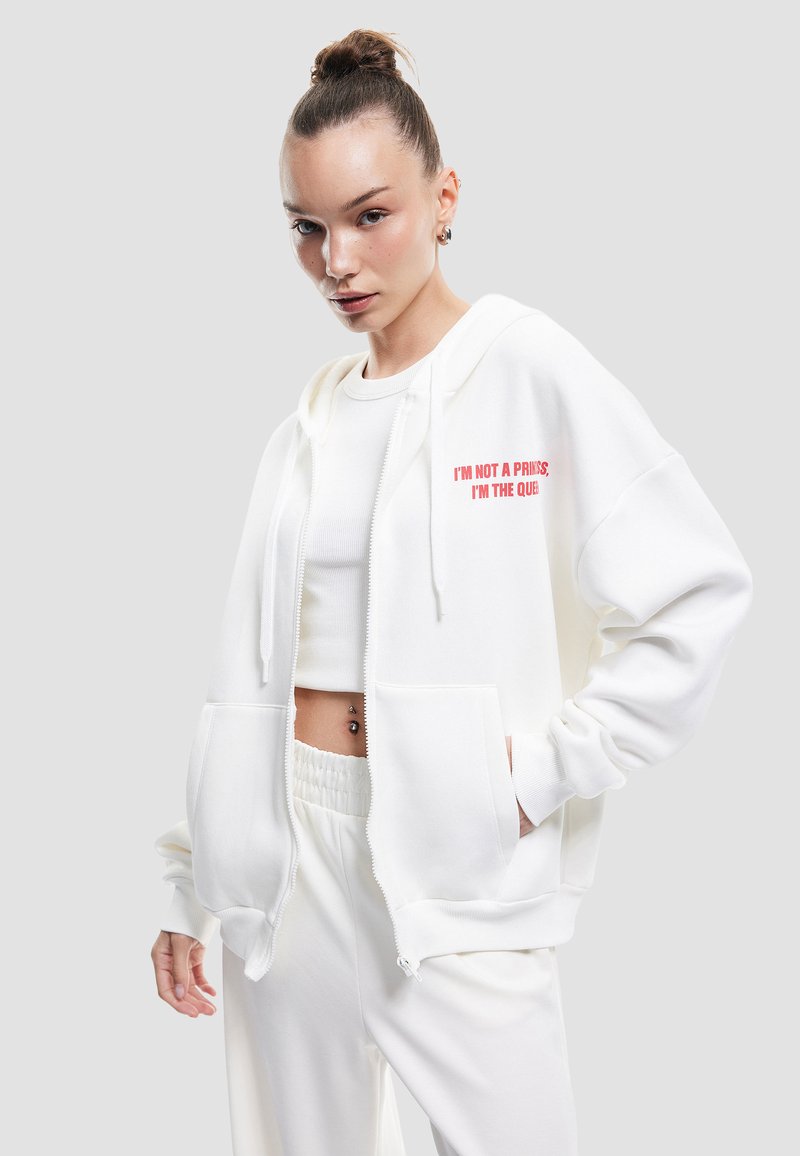 Weißer Zip-Hoodie mit zwei vorderen Taschen und Kapuze mit Kordelzug, mit pinkem Text "ICH BIN KEINE PRINZESSIN, ICH BIN DIE KÖNIGIN" auf der linken Brust.