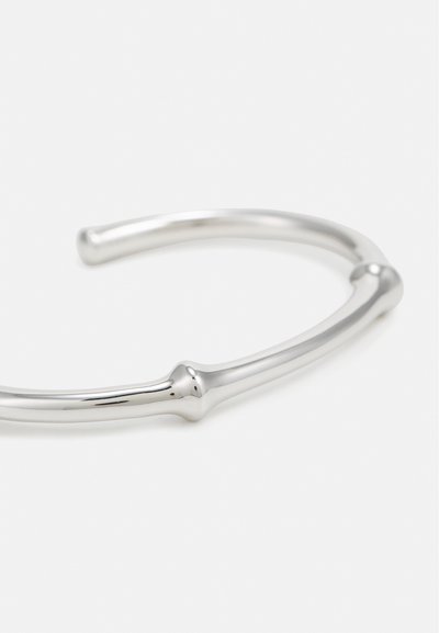 Bracciale a fascia in metallo d'argento con un design liscio e minimalista, caratterizzato da forme arrotondate e sottili dettagli che ricordano le giunture del bambù.