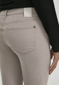 Bež skinny traperice napravljene od mješavine pamuka, s suptilnom teksturom, uskim krojem i stražnjim džepovima s izraženim detaljima šivanja.