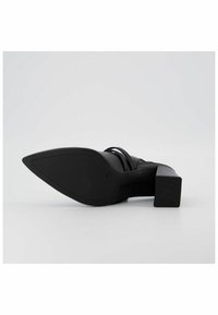 Chaussure à talons hauts noire avec un bout pointu et un large talon bloc, présentant un design à lanières et une texture en cuir lisse. Logo sur la semelle.