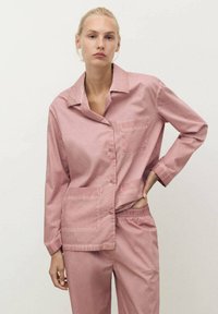 Rosa bomullspyjamas-set med en kragad knäppskjorta med bröstfick och byxor med elastisk midja. Strukturen verkar jämn och lätt.