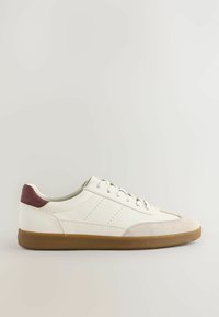 Hvid sneaker med en glat læderoverdel, gummisål og en maroon ruskindsdetalje ved hælen. Har perforeringer og runde snørebånd.