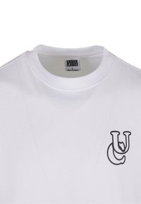 Balta kokvilnas T-kreklu ar melnu izdrukātu "UC" logo kreisajā krūšu daļā. Ar apaļu kakla dizainu. Etiķete norāda "URBAN CLASSICS", izmērs L.