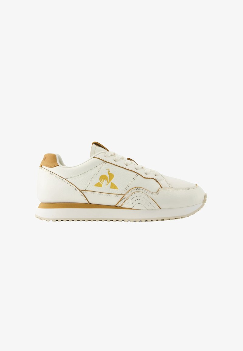 Des baskets en cuir blanc présentent des accents dorés et un design unique. La semelle est légère, texturée pour une meilleure adhérence, et comprend des détails cousus.