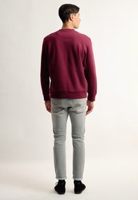 Sudadera burdeos con cuello redondo y dobladillo acanalado, combinada con jeans gris claro y botas negras hasta el tobillo, vista desde la parte posterior.