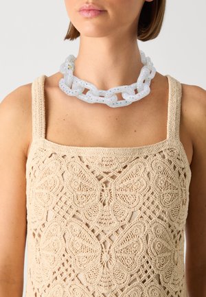 Collana in catena translucida con finitura lucida, caratterizzata da glitter incorporati; indossata su un top in maglia beige con un motivo a farfalla.