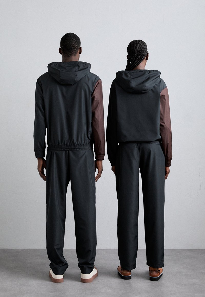 Vestes à capuche noires et marron avec des ceintures élastiques, assorties à des pantalons noirs amples. Texture lisse avec des manches contrastantes.