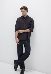 Dunkelblause mit hochgekrempelten Ärmeln, kombiniert mit dunklen Jeans und schwarzen Schuhen. Einfaches Design, lässige Passform, einheitliches Farbschema.