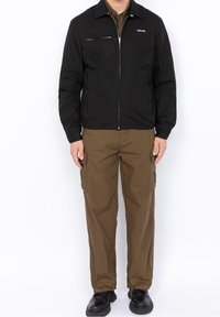 Black zip-up jacket with a collar and a chest pocket, paired with brown cargo pants featuring side pockets. Worn with black shoes.